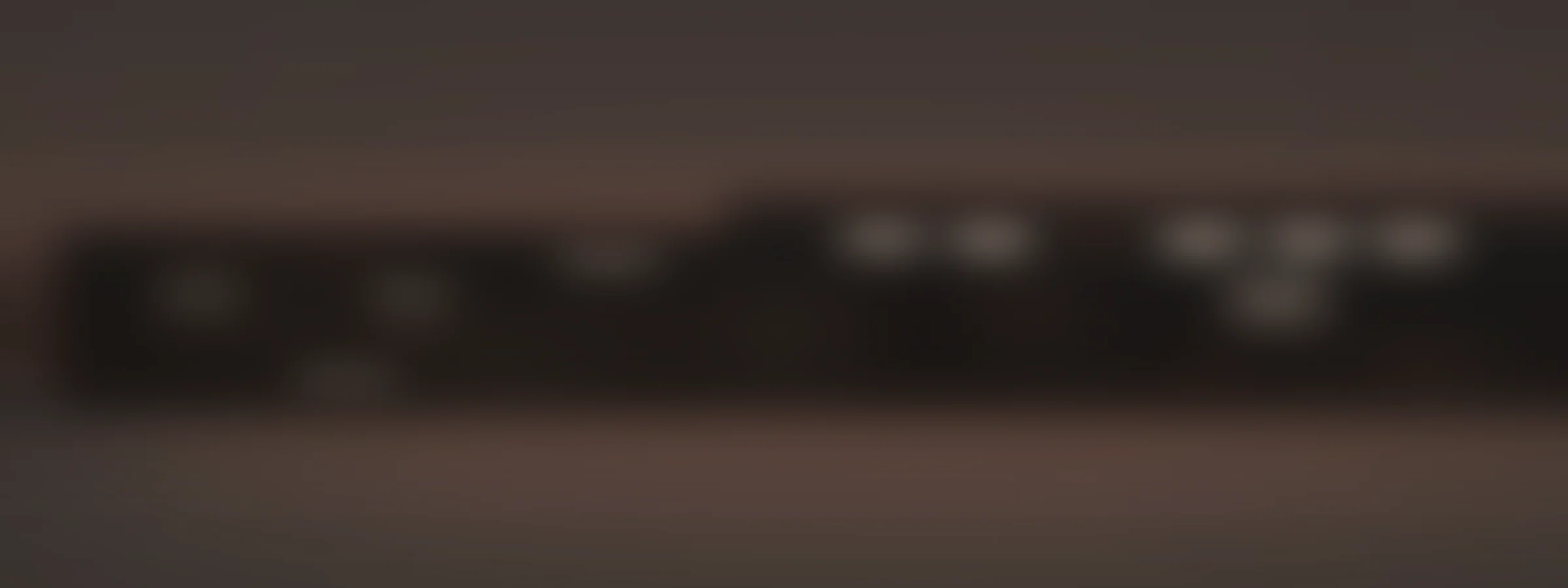 A wide dark atmospheric field in warm charcoal and clay, with distant architecture out of focus.