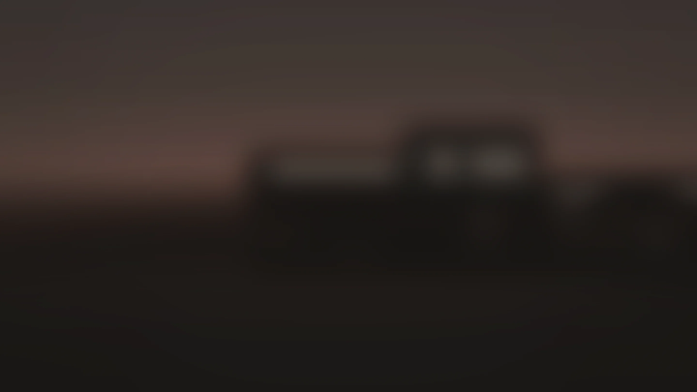 A dark atmospheric field in warm charcoal and clay, with architecture far out of focus at dusk.